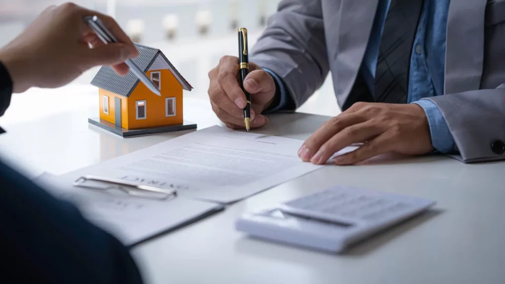 Mini yellow house on table next to businessmen signing timeshare agreement | Wesley Financial Group